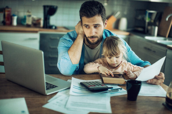 A dad sits with his daughter on his lap while looking worried at a computer