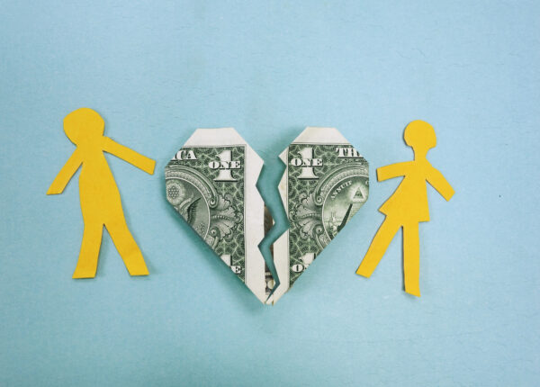 Two paper cutouts of people on either side of a broken heart made of dollar bills.