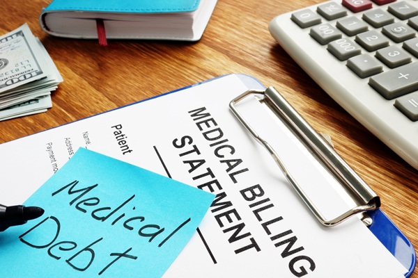 Clipboard with a medical billing statement and a sticky note labeled “Medical Debt,” surrounded by cash, a notebook, and a calculator, representing the financial burden of healthcare costs and potential bankruptcy considerations.