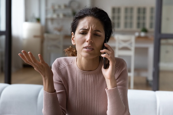 A young woman on the phone, looking frustrated as she speaks with a debt collector.